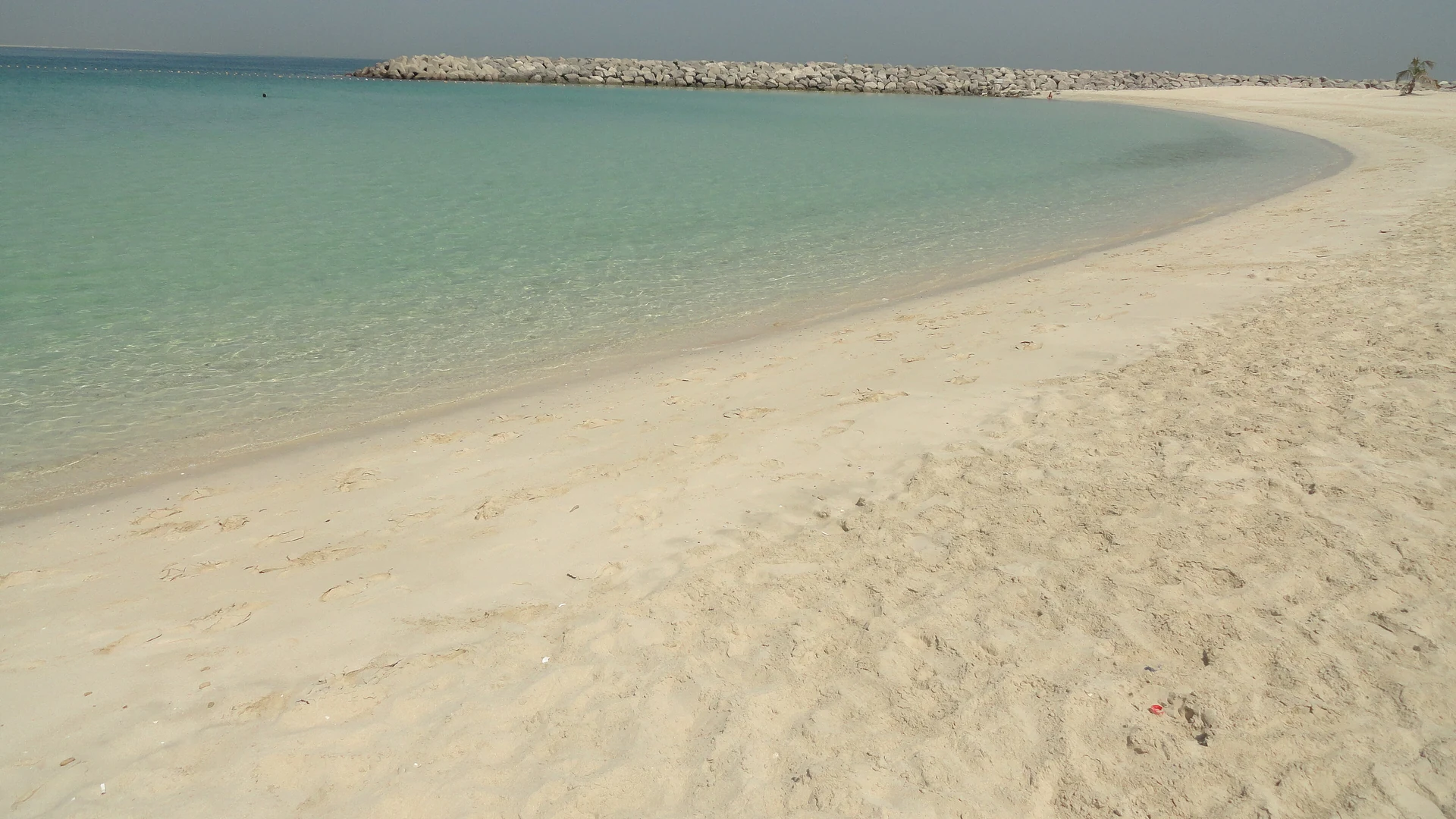 A curve of pale sand and calm turquoise water at Al Mamzar Beach Park in Dubai, with a rock breakwater in the distance