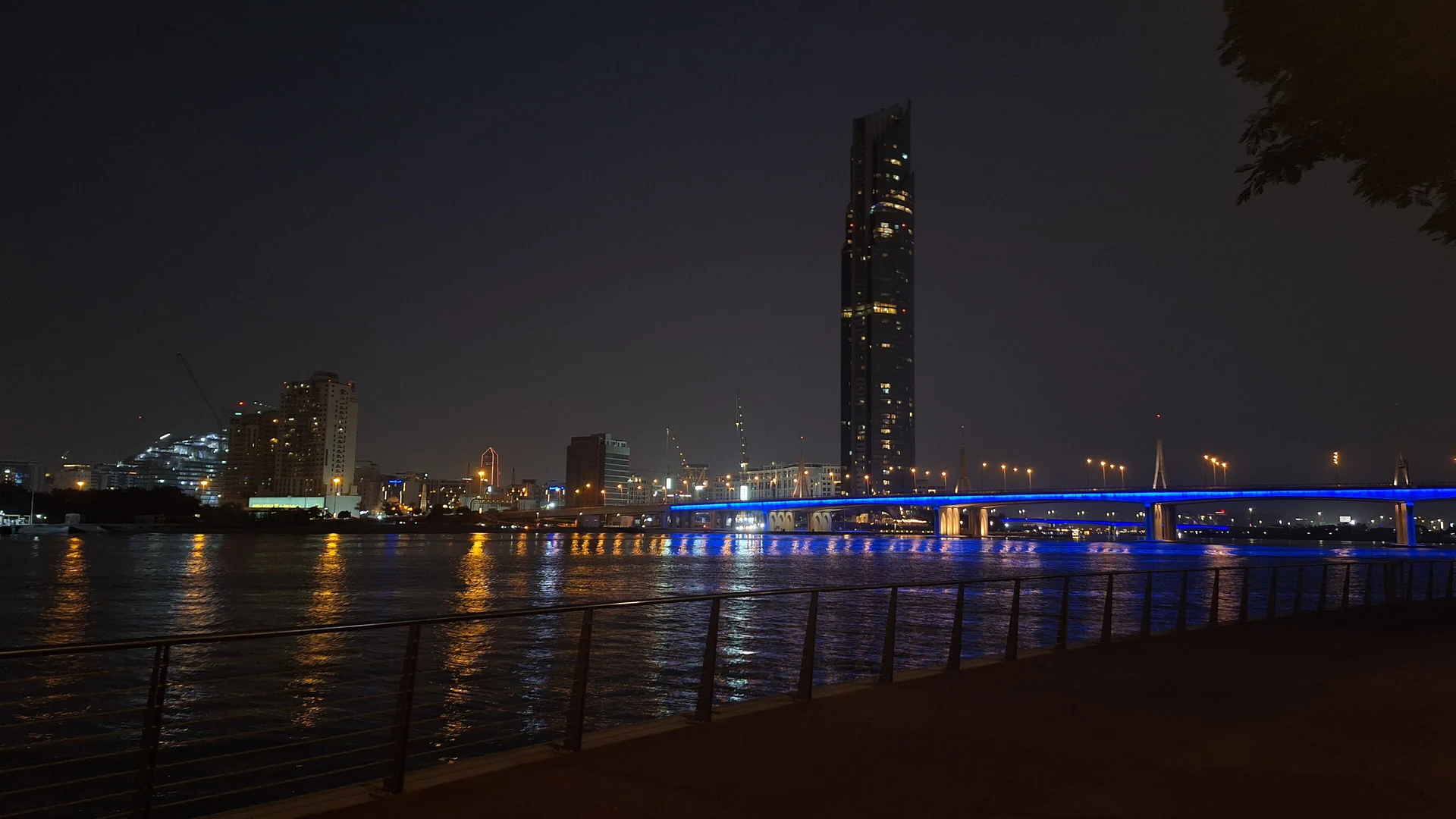 The illuminated Business Bay Crossing bridge over Dubai Canal at night, with a tall hotel tower behind