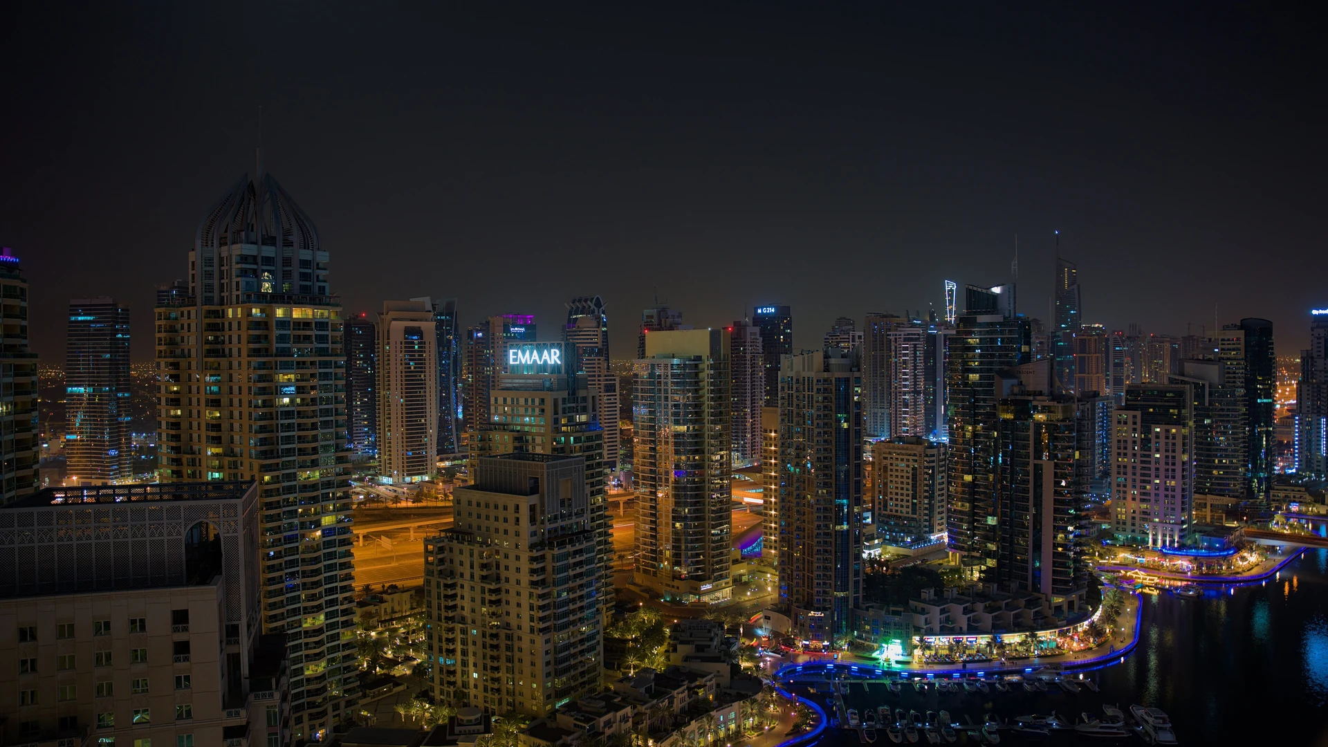 Dubai Marina's high-rise towers lit up at night above the illuminated waterfront promenade and moored yachts