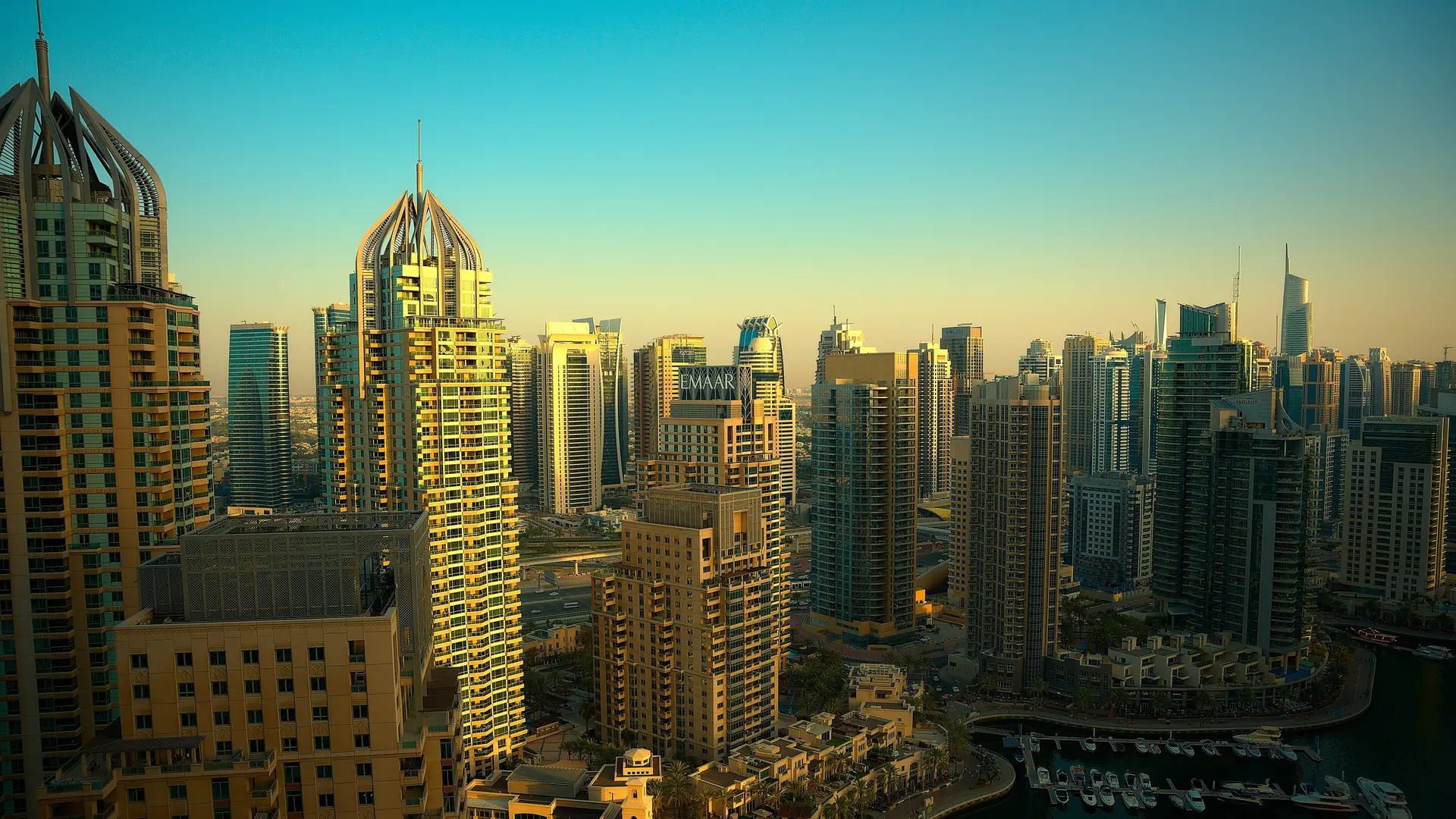 Dubai Marina's towers in warm late-afternoon light under a clear sky, with yachts in the marina below