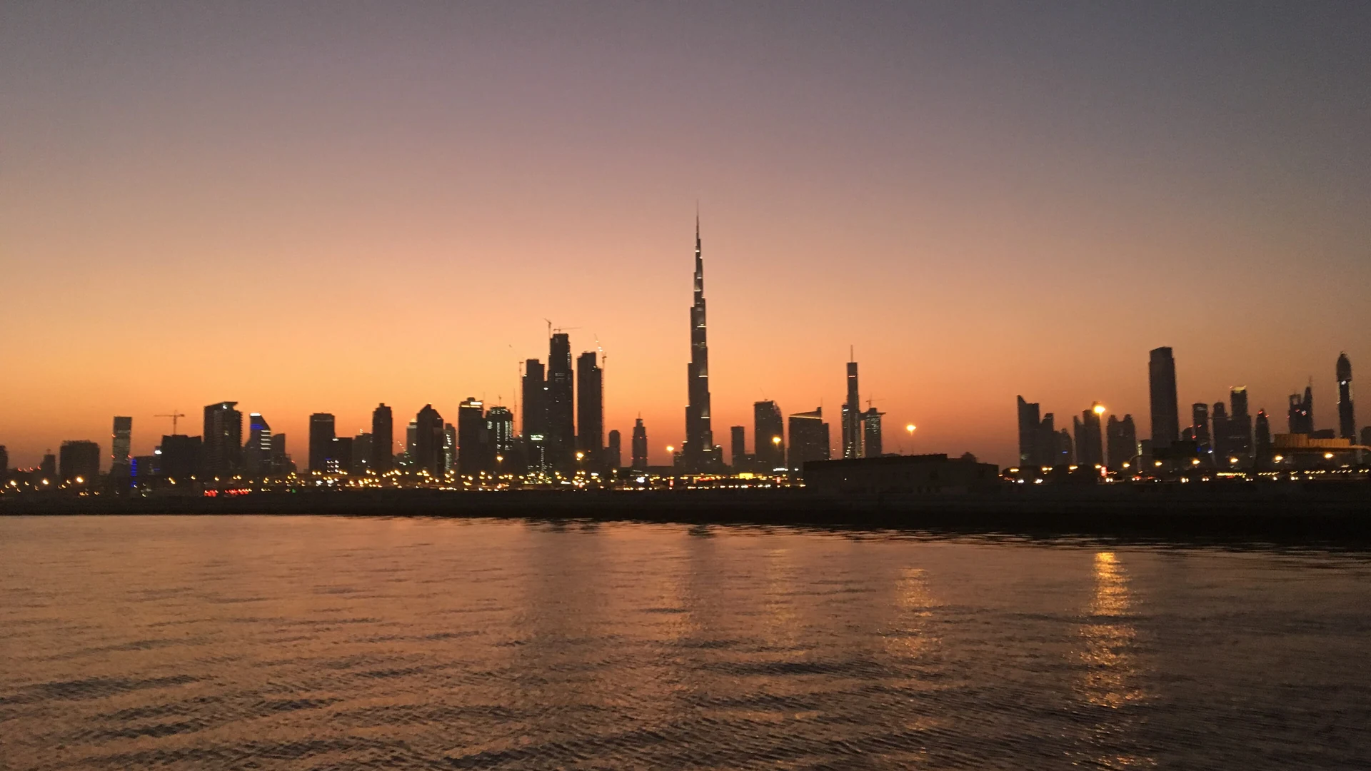 The Burj Khalifa silhouetted against an orange dusk sky above the Dubai skyline and waterfront