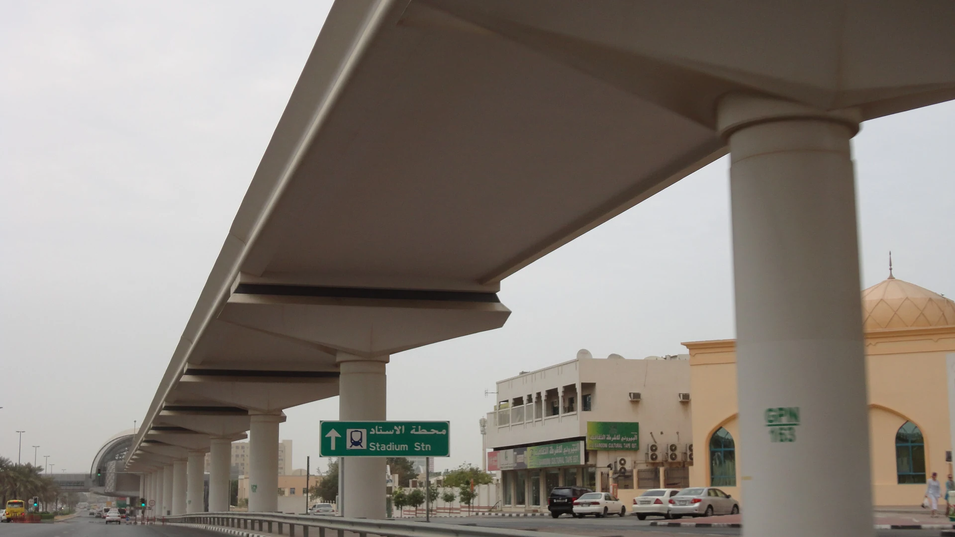 Dubai Metro's elevated concrete viaduct on pillars above a road in Deira, with a road sign pointing to Stadium Station